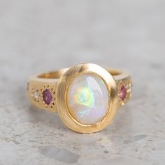 Our Sun Punch Ring has been set with a Crystal Opal from Coober Pedy and bead set with Pink Sapphires, G/VS White Diamonds and Salt & Pepper Diamonds in the band. Opal measures approx. 10 x 8mm. There are a total of three birlliant cut pink sapphires and four brilliant cut diamonds. Band width tapers from approx. 6mm to 3.4mm at the back of the band. Gold weight approx. 11g in 14ct, 12.6g in 18ct. This ring is pictured with a matte finish. For a polished finish please leave a note at the checkout. Please note, we will match the opal as close to the image as possible. Each opal is unique and may vary in appearance and colour from what is depicted on the site. Opal Wedding Ring, Pink Sapphire Ring, Coober Pedy, Crystal Opal, Bead Set, Jewelry Lookbook, Salt And Pepper Diamond, Opal Crystal, White Diamonds