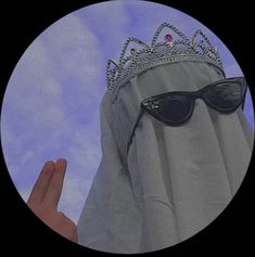 a person wearing sunglasses and a tiara standing in front of a curtain with the sky behind them