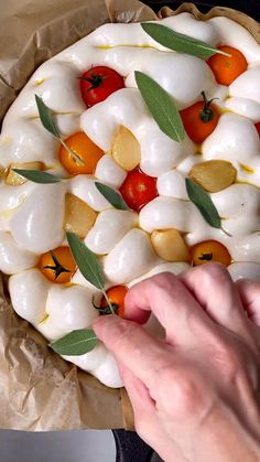 a person is placing toppings on top of a pizza crust with leaves and tomatoes