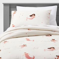 a bed with white sheets and pink mermaids on it, along with two pillows