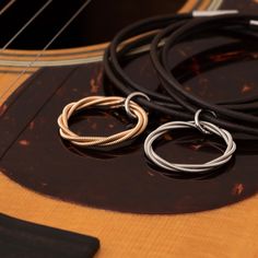 two silver and gold rings sitting on top of an acoustic guitar strings next to a black cord