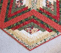 a red and green quilted table runner on top of a white rug with flowers