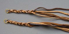 two brown and black braided ties on a gray surface with gold rings hanging from the ends