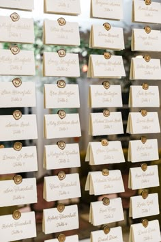 wedding place cards are hanging on a glass wall in front of a window with gold buttons