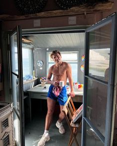 a shirtless man sitting on top of a chair in front of a window next to a desk