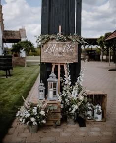 a wooden sign sitting on top of a brick floor next to flowers and lanterns in front of a building