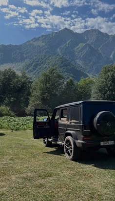 a black jeep parked on top of a lush green field next to a mountain range