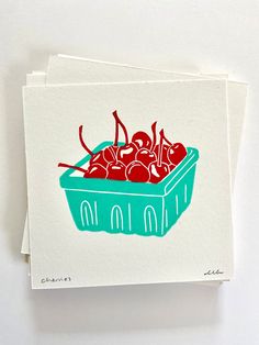 two greeting cards with cherries in a blue bowl on white paper, one has red ink and the other has green ink