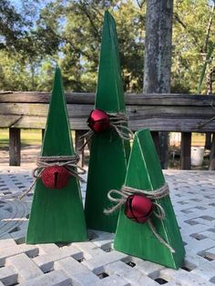 three small wooden christmas trees with red balls tied to them, sitting on a table