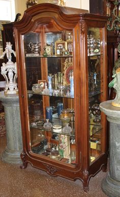 an antique china cabinet with glass doors in a room filled with statues and vases