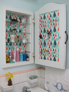 an open medicine cabinet in a bathroom with colorful wallpaper on the walls and behind it is a sink