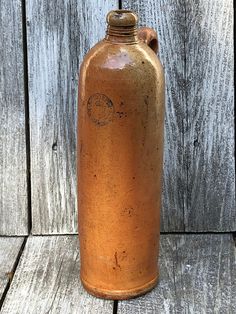 an old brown flask bottle sitting on top of a wooden table next to a wall