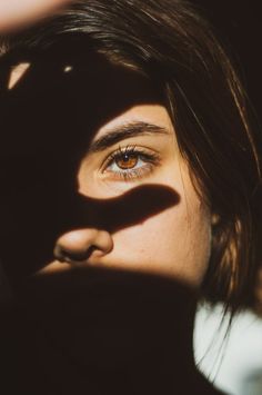 a woman's face is shown with the shadow of her hand over her eye