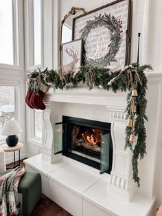 a fireplace decorated with christmas garland and stockings for the mantel, in front of a large window