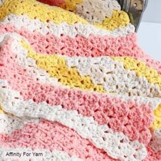 a crocheted blanket sitting on top of a bed next to an apple and book