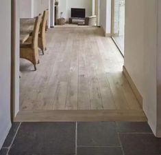 an empty room with wooden floors and white walls, leading to a long dining table