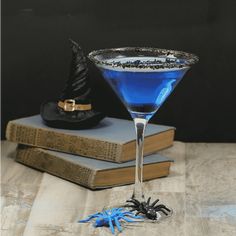 a blue drink in a martini glass with a spider on the table next to it