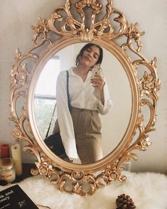 a woman taking a selfie in front of a mirror with a book and pine cone