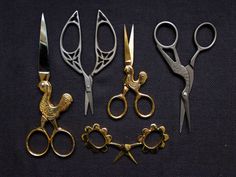 five pairs of scissors are sitting on a black surface, one is gold and the other is silver