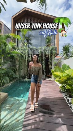 a woman standing in front of a swimming pool with palm trees and greenery around her