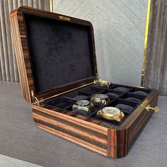 an open wooden watch box sitting on top of a gray table next to a wall