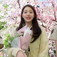 a woman holding flowers in front of a cherry blossom tree with two uniformed men behind her