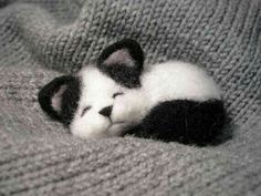 a small black and white kitten laying on top of a gray blanket next to a stuffed animal