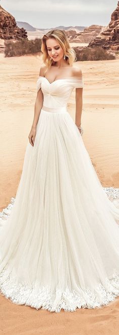 a woman in a white wedding dress standing on the sand with mountains in the background