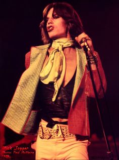 the woman is singing on stage with her microphone up to her ear and wearing a scarf around her neck