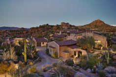 an aerial view of a home surrounded by cactus and rocks at sunset with mountains in the background