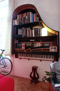 a piano shelf with books and musical instruments on it in front of a window next to a bicycle