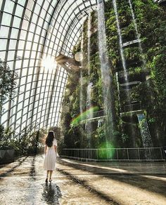 a woman in a white dress is walking through a waterfall tunnel at gardens by the bay