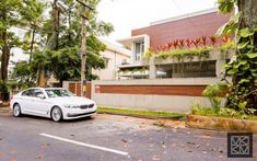 a white car is parked in front of a house with trees and bushes on the side