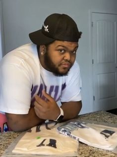 a man sitting at a table with some t - shirts on it