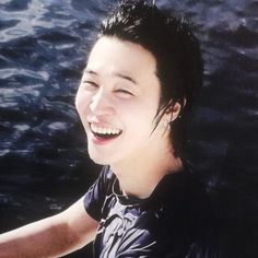 a young man smiles while sitting on a boat in the water with his eyes closed