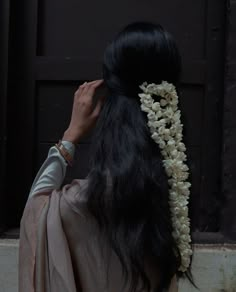 a woman with long black hair wearing a white flowered headpiece in front of a door