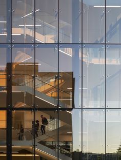 two people walking up and down the stairs in front of a building with glass walls