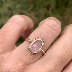 a woman's hand with a ring on it that has a pink stone in the middle