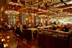 people are sitting at tables in a restaurant with chandeliers hanging from the ceiling