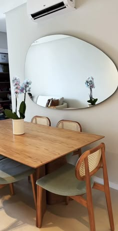 a wooden table with four chairs and a round mirror on the wall in front of it