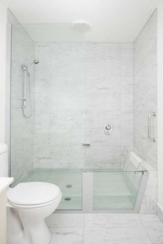 a white bathroom with marbled walls and flooring, including a walk in shower