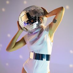 a woman in a white dress holding a disco ball up to her face with both hands