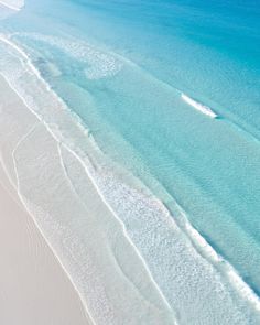 an aerial view of the beach and ocean with white sand, blue water and waves