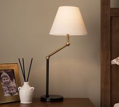 a lamp on a table next to a white vase with a black and gold handle