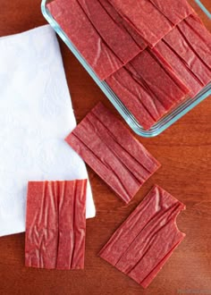 pieces of red food sitting on top of a wooden table