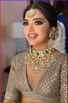 a woman in a gold and green outfit with jewelry on her neck, smiling at the camera