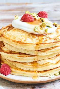 a stack of pancakes topped with whipped cream and raspberries