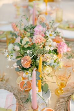 an arrangement of flowers and candles on a table with plates, glasses and napkins