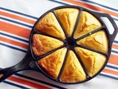 a cast iron skillet filled with food on top of a striped table cloth next to an orange and white towel