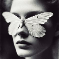 a black and white photo of a woman with a butterfly on her face in front of her eyes